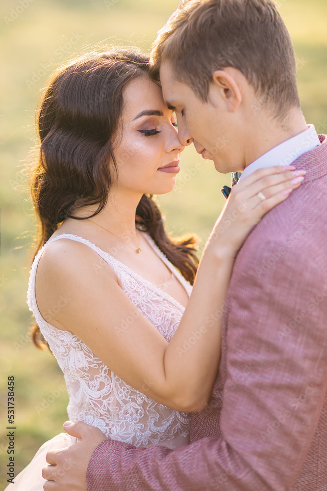 Romantic newlyweds hug and kiss in a field at sunset