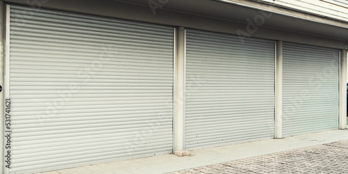 Building facade with closed steel shutters outdoors. Market or store gate is closed with rolling blinds.