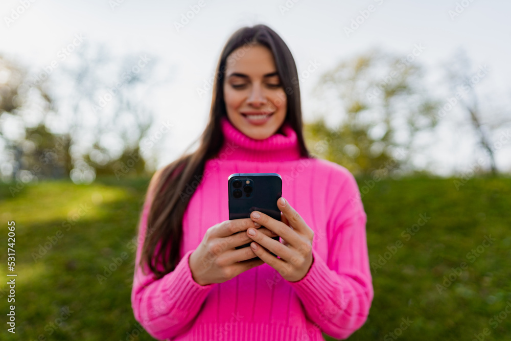 young smiling woman in pink sweater walking in green park using phone young smiling woman in pink sweater walking in green park using phone