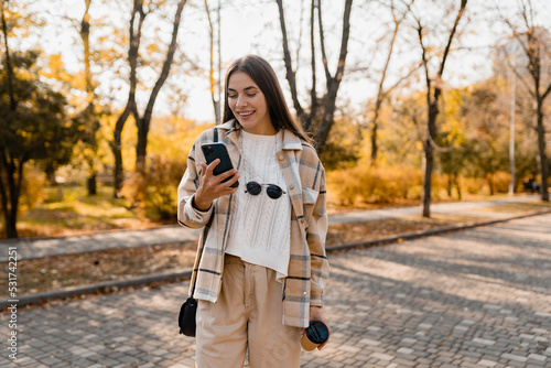 attractive young woman walking in autumn wearing jacket using phone photo