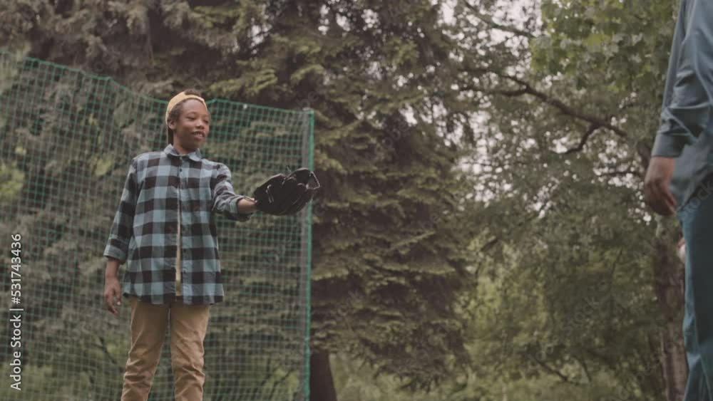 Medium slowmo of Black man teaching his 12 year old son to catch baseball with glove having training outdoors in park on warm summer day Medium slowmo of Black man teaching his 12 year old son to catch baseball with glove having training outdoors in park on warm summer day