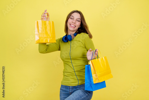 Happy young teenage girl holding shopping bags and standing on yellow background.Retail fashion sale, mall boutique discounts bargains and gifts concept.