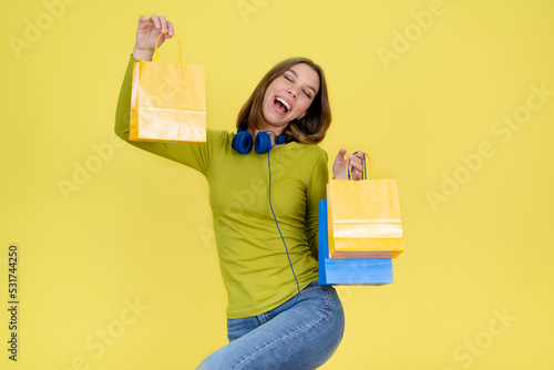 Happy young teenage girl holding shopping bags and standing on yellow background.Retail fashion sale, mall boutique discounts bargains and gifts concept.