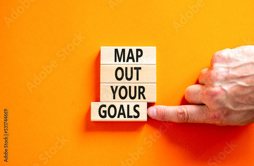 Support and map out your goals symbol. Concept words Map out your goals on wooden blocks on beautiful orange table orange background. Businessman hand. Business, support and map out your goals concept