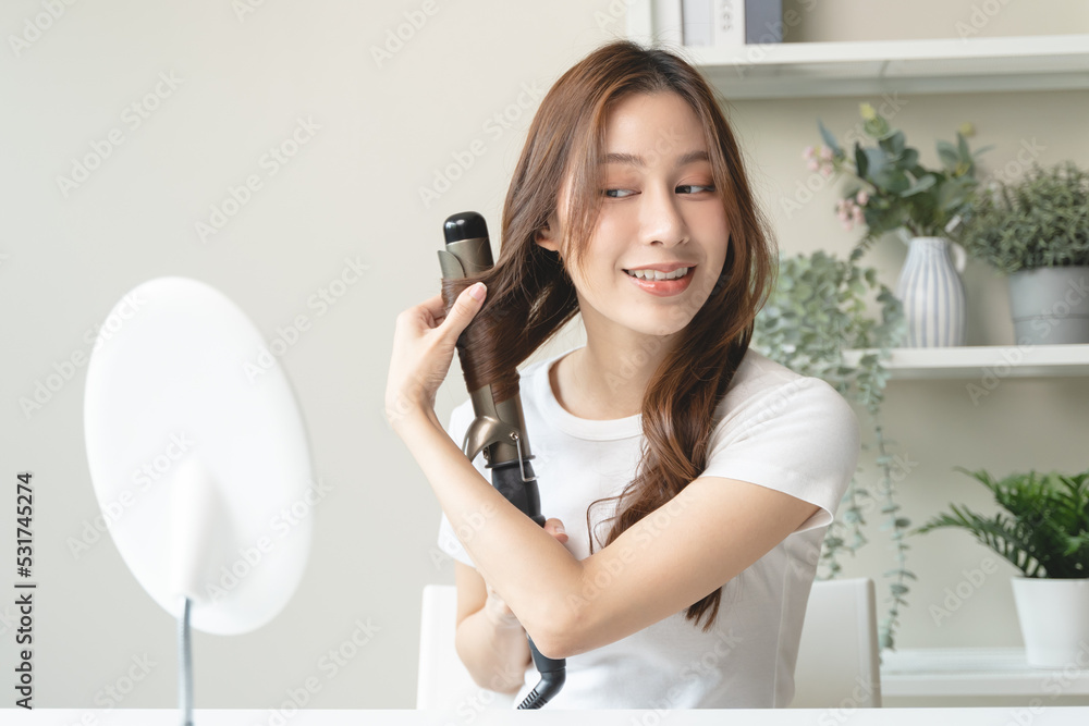 women hairdo makeup routine, Young woman looking at the mirror and using iron hair curling curly long hair at home. women hairdo makeup routine, Young woman looking at the mirror and using iron hair curling curly long hair at home.