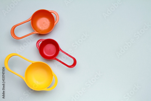 Colorful plastic measuring spoons and measuring cups on bright background top view with space for text
