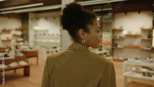 A stylish African-American woman in a jacket walks into a luxury shoe store