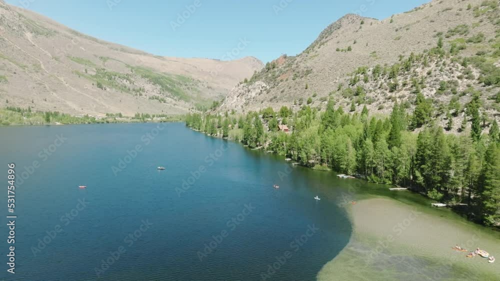 Crystal clear glacier water surrounded by tall green pine trees with high summit Sierra Nevada peaks background. Aerial of beautiful scenic mountain lake with Alpine landscapes on sunny warm fall day Crystal clear glacier water surrounded by tall green pine trees with high summit Sierra Nevada peaks background. Aerial of beautiful scenic mountain lake with Alpine landscapes on sunny warm fall day