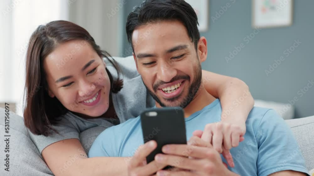 Happy, love and a couple on a phone, kiss and streaming a online with social media or funny meme. Married asian woman and man relax on home living room sofa watching content on the web or internet Happy, love and a couple on a phone, kiss and streaming a online with social media or funny meme. Married asian woman and man relax on home living room sofa watching content on the web or internet