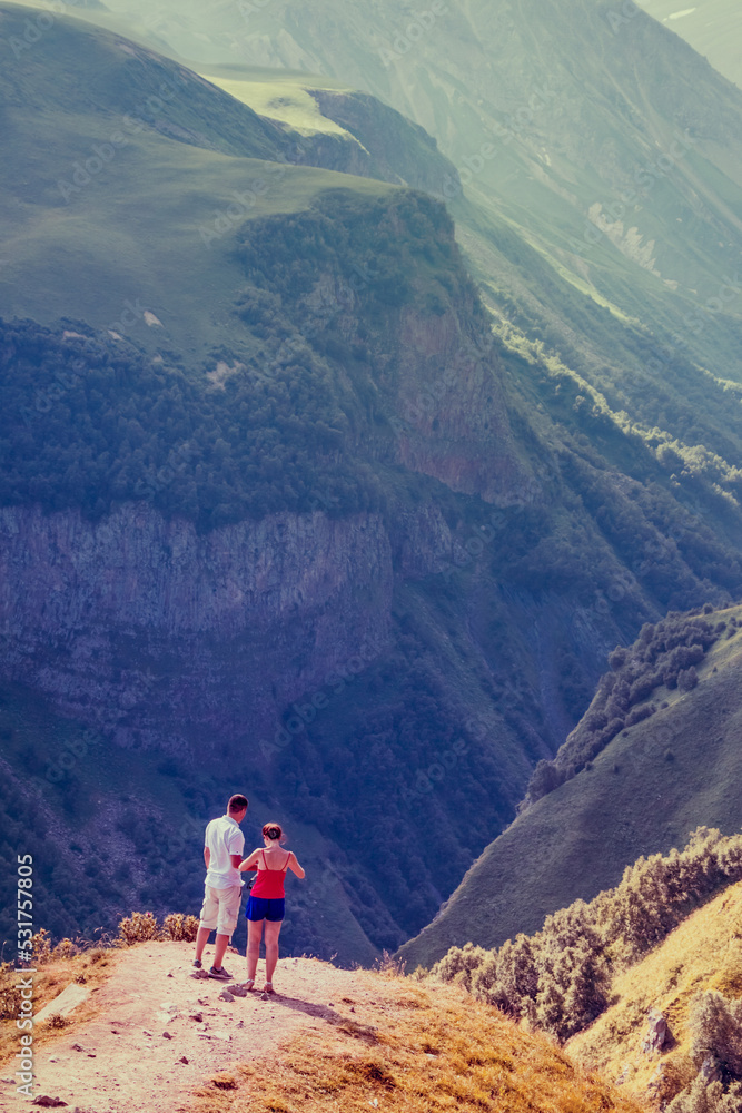 A couple on a journey looks at the majestic mountains. Beautiful mountains, breathtaking view. A tourist watches the setting sun in the mountains. Travel and active lifestyle