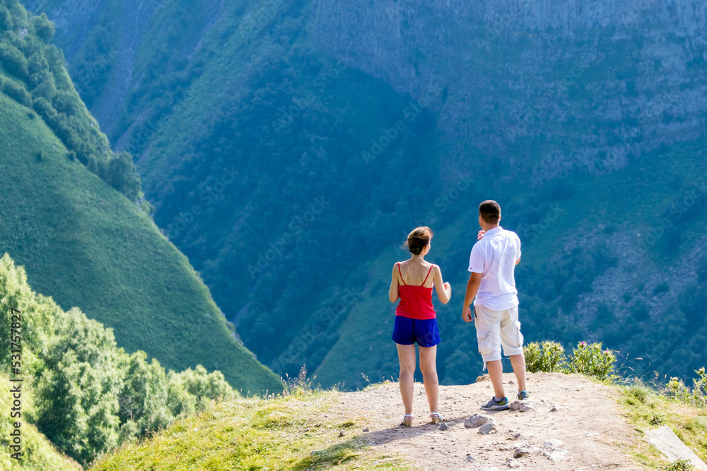 Naklejka premium A couple on a journey looks at the majestic mountains. Travel and active lifestyle. Beautiful mountains, breathtaking view. A tourist watches the setting sun in the mountains