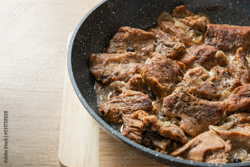 Fried beef with onions and spices in a frying pan on a light texture background. Meat recipe. Juicy grilled steak, close-up. Place for text, space for copy.