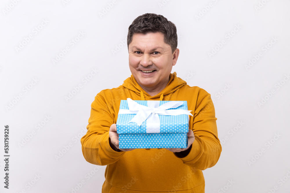 Portrait of positive generous man smiling and giving gift box, sharing holiday present, charity concept, wearing urban style hoodie. Indoor studio shot isolated on white background. Portrait of positive generous man smiling and giving gift box, sharing holiday present, charity concept, wearing urban style hoodie. Indoor studio shot isolated on white background.