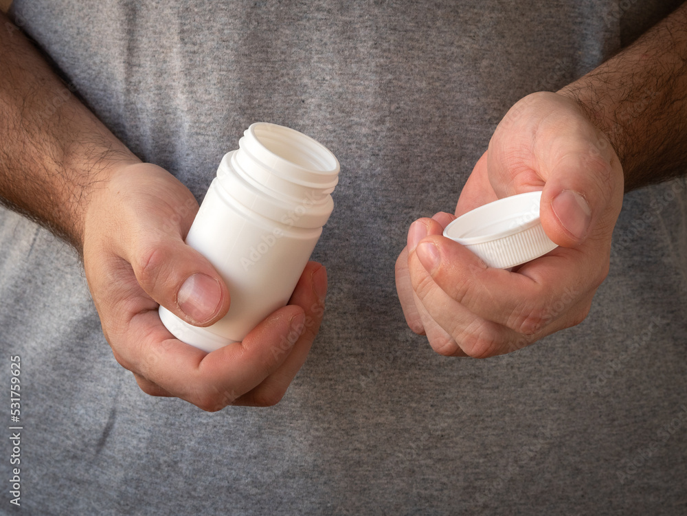 Men's hands open a plastic white jar with medicines or multivitamins. Treatment and prevention of diseases Men's hands open a plastic white jar with medicines or multivitamins. Treatment and prevention of diseases