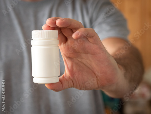 The man holds and shows in his hand a white jar with a medicine or multivitamins, or a dietary supplement. Treatment and prevention of diseases