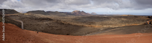 Panoramic image of the mountains of the Timanfaya National Park shot from the Islote de Hilario. Two buses visible taking the tourists on a roundtrip through the park. photo