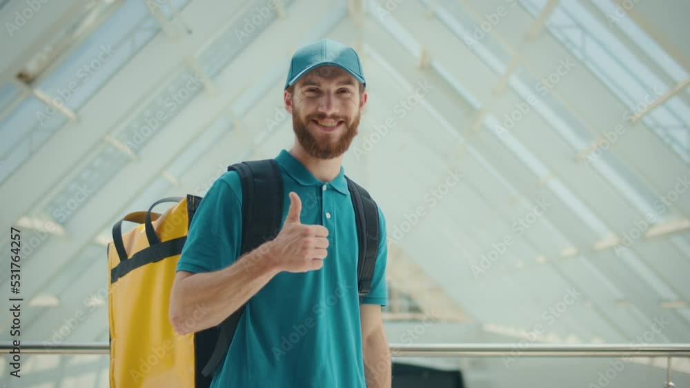 Portrait of Handsome Delivery Person in Uniform and With a Thermal Backpack. Smiling Courier Showing Thumbs. Courier Working in Logistics Distribution Center, Delivering Online Orders. Portrait of Handsome Delivery Person in Uniform and With a Thermal Backpack. Smiling Courier Showing Thumbs. Courier Working in Logistics Distribution Center, Delivering Online Orders.