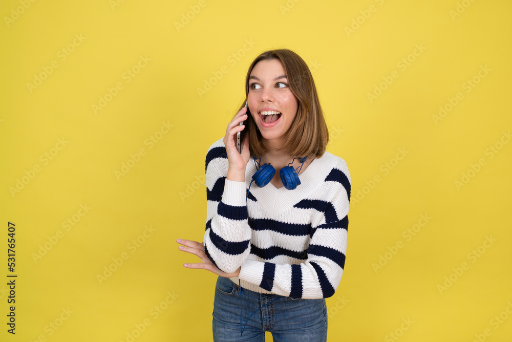 Portrait of cute happy teenage girl wearing talking on mobile phone and smiling over yellow background. Copy space. Portrait of cute happy teenage girl wearing talking on mobile phone and smiling over yellow background. Copy space.