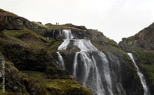 Two hikers positioned above the 198m high Glymur Waterfall. Located in southwestern Iceland.