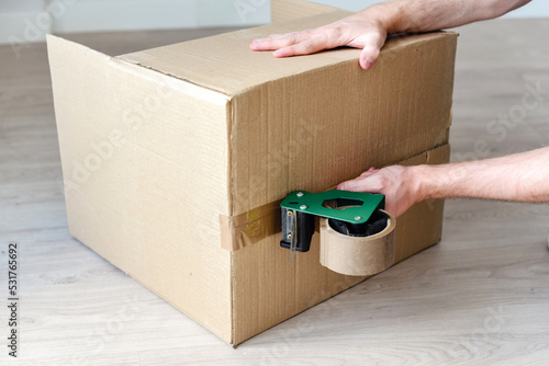 Detalle de un hombre usando una herramienta para precintar una caja de cartón con cinta adhesiva marrón. Embalaje de cajas de mudanza. photo