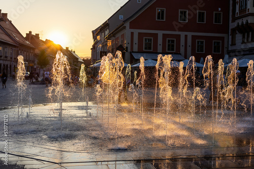 Water spraying from fountain in city of Maribor, Slovenia, at sunset. Splashing droplets from several geysers backlit by evening sun. Concept of keeping moisture in towns and streets.