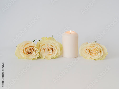 Three roses next to a burning white candle on a white background with copy space for text.