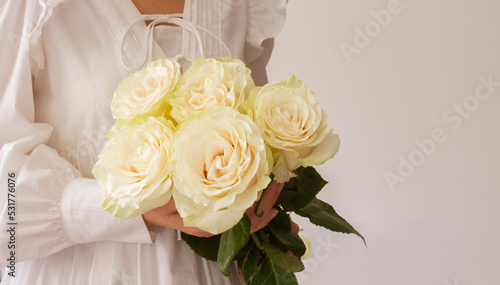Young woman in a white dress holding bouquet of flowers on white background with copy space for text