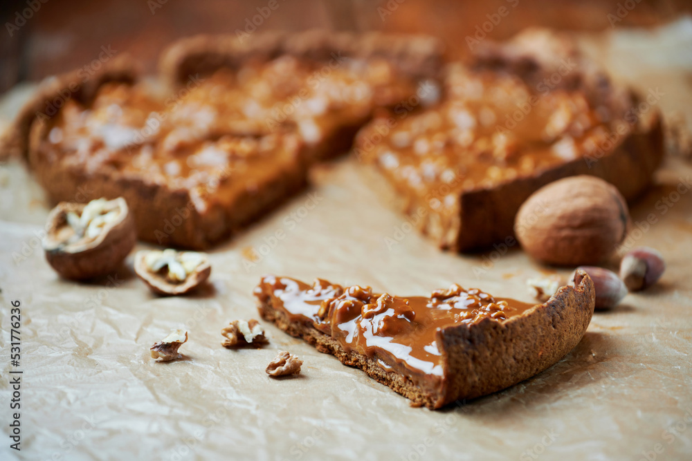 Slice of tart with caramel and walnut on baking paper on wooden table. Autumn thanksgiving dessert. Slice of tart with caramel and walnut on baking paper on wooden table. Autumn thanksgiving dessert.