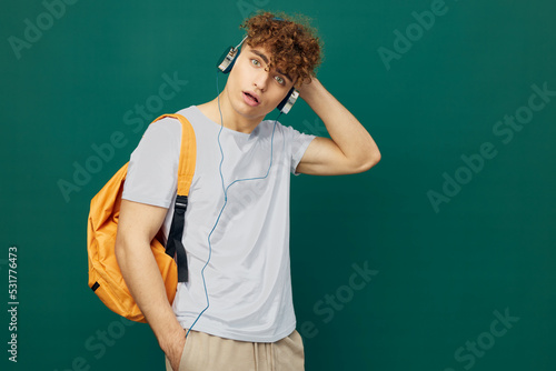 horizontal portrait of a handsome man with curly hair, standing on a green background in a gray T-shirt, and looking in surprise to the side, holding his headphones on his head with his hand © Tatiana