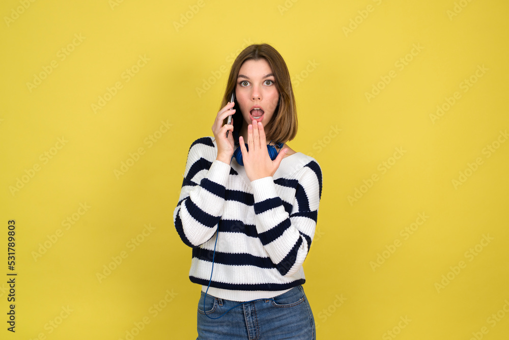 Portrait of cute happy teenage girl wearing talking on mobile phone and smiling over yellow background. Copy space. Portrait of cute happy teenage girl wearing talking on mobile phone and smiling over yellow background. Copy space.