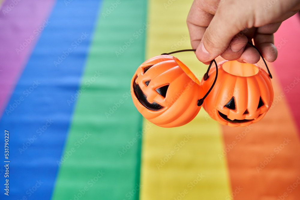 Two Halloween pumpkin head baskets hanging by fingers with lgbt pride flag on background Stock Photo