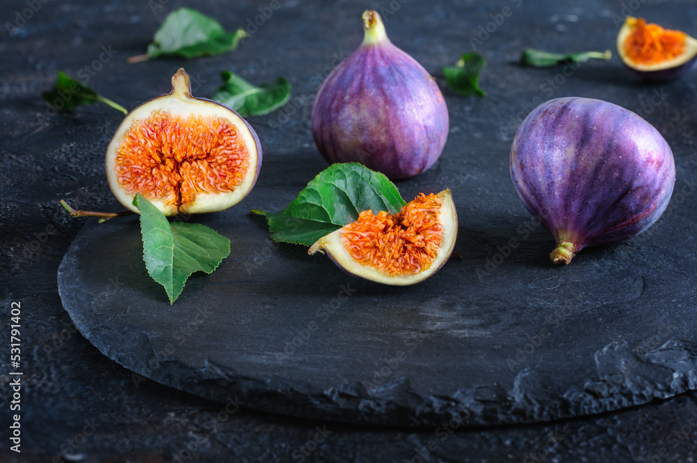 Fresh figs whole and cut into pieces on black slate. Autumn fruits. Front view, selective focus, daylight Fresh figs whole and cut into pieces on black slate. Autumn fruits. Front view, selective focus, daylight