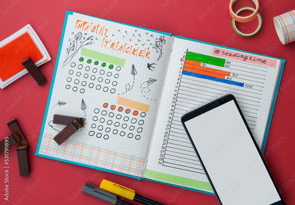 Bullet journal page with handwriting, Bullet Journal-style notebook is opened on habit and book tracker page with smartphone Bullet journal page with handwriting, Bullet Journal-style notebook is opened on habit and book tracker page with smartphone