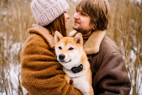 Cute young couple having fun in the winter park with their dog on bright day.Man and woman are relaxing