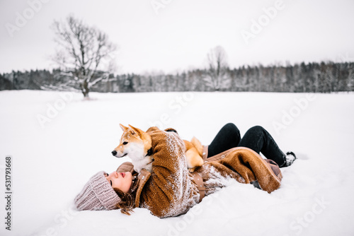 Cute young girl is having fun in winter park with her dog on bright day. Woman relaxing outdoors