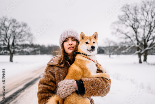 Cute young girl is having fun in winter park with her dog on bright day. Woman relaxing outdoors
