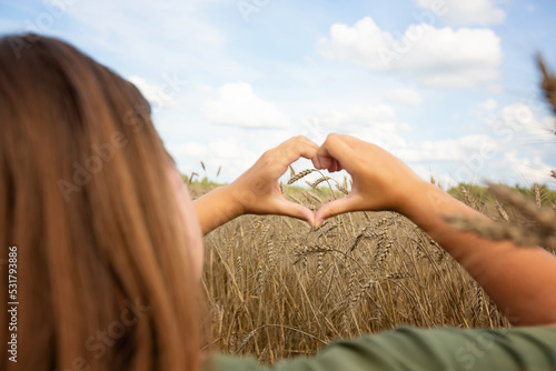 Women's hands in the shape of a heart on the background of the sky and a field with ears of corn. Hands in the shape of a love heart.