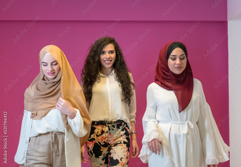 three Muslim women in hijab in a modern clothes pose against a pink background