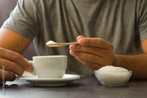 Male hand holding wooden spoon with sugar over cup of coffee or tea. Stop sugar. Campaign against diabetes, obesity, dental caries. Reduce sugar intake.