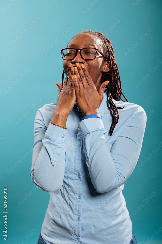 Exhausted african american person catching a yawn while putting hand over mouth. Tired sleepy young adult woman yawning mouth wide open because of fatigue from overtime work Exhausted african american person catching a yawn while putting hand over mouth. Tired sleepy young adult woman yawning mouth wide open because of fatigue from overtime work