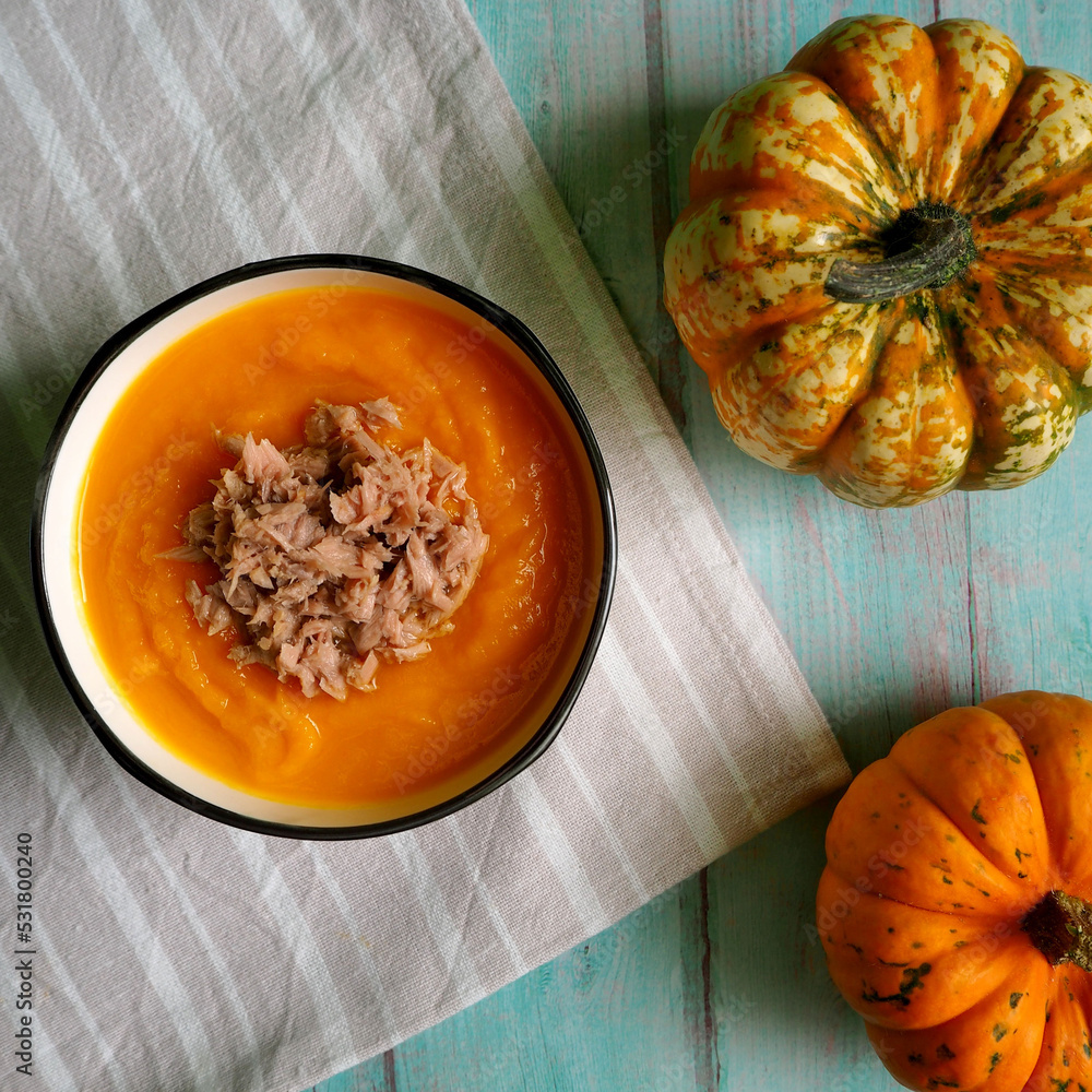 pumpkin soup puree in a round plate with tuna and two small pumpkins stand side by side on a blue wooden table. view from above. diet pumpkin soup puree in a round plate with tuna and two small pumpkins stand side by side on a blue wooden table. view from above. diet