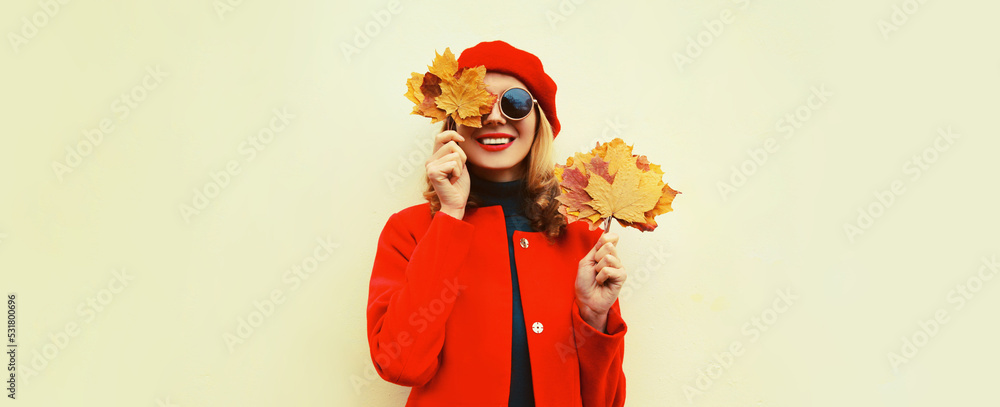 Autumn portrait of happy smiling young woman with yellow maple leaves wearing red french beret on gray background Autumn portrait of happy smiling young woman with yellow maple leaves wearing red french beret on gray background