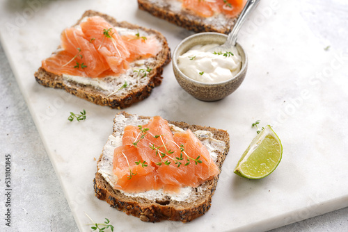 Wholewheat bread sandwiches with cream cheese and smoked salmon on marble board with lime slices and sour cream