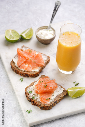 Wholewheat bread sandwiches with cream cheese and smoked salmon on marble board with orange juice, lime slices and sour cream
