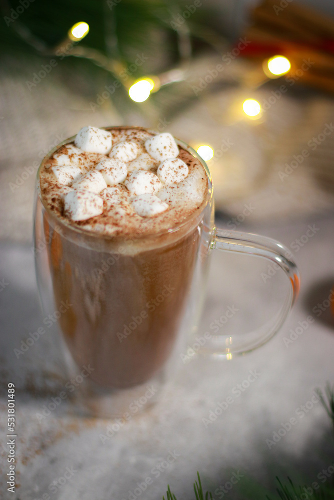 hot chocolate in a glass mug with mini marshmallows on grey table, blurred lights background hot chocolate in a glass mug with mini marshmallows on grey table, blurred lights background