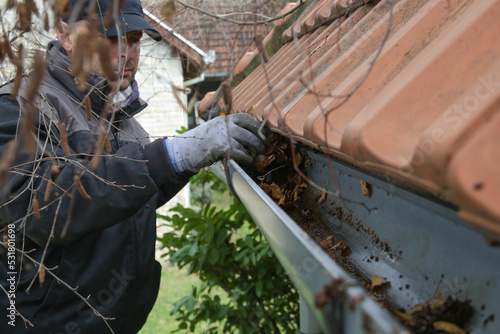 Man cleaning the gutter from autumn leaves before winter season. Roof gutter cleaning process. 