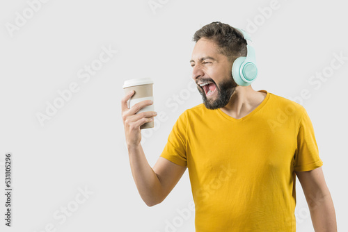 A latin adult man with yellow shirt on white background is singing while he is looking his coffee cup