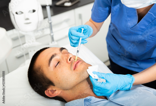 Woman doctor giving rejuvenating injections with syringe for facial correction to male patient in beauty clinic
