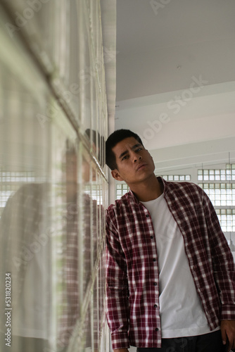 Joven estudiante latino recostado sobre un muro de bloques de vidrio 