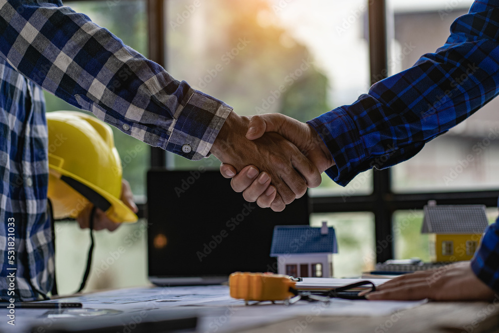 Architects and construction engineers shake hands while working as a team and collaborating ideas after finishing a deal on office blueprints and tabletop house plans. Architects and construction engineers shake hands while working as a team and collaborating ideas after finishing a deal on office blueprints and tabletop house plans.